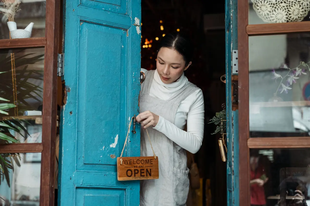 A shop owner hanging an OPEN sign on a blue front door