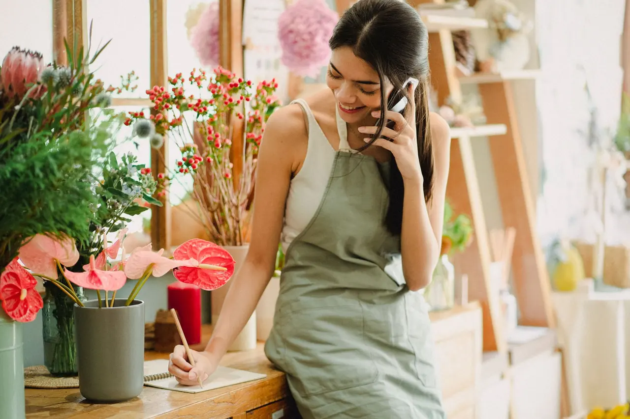 A florist taking a phone call while writing an order at her counter